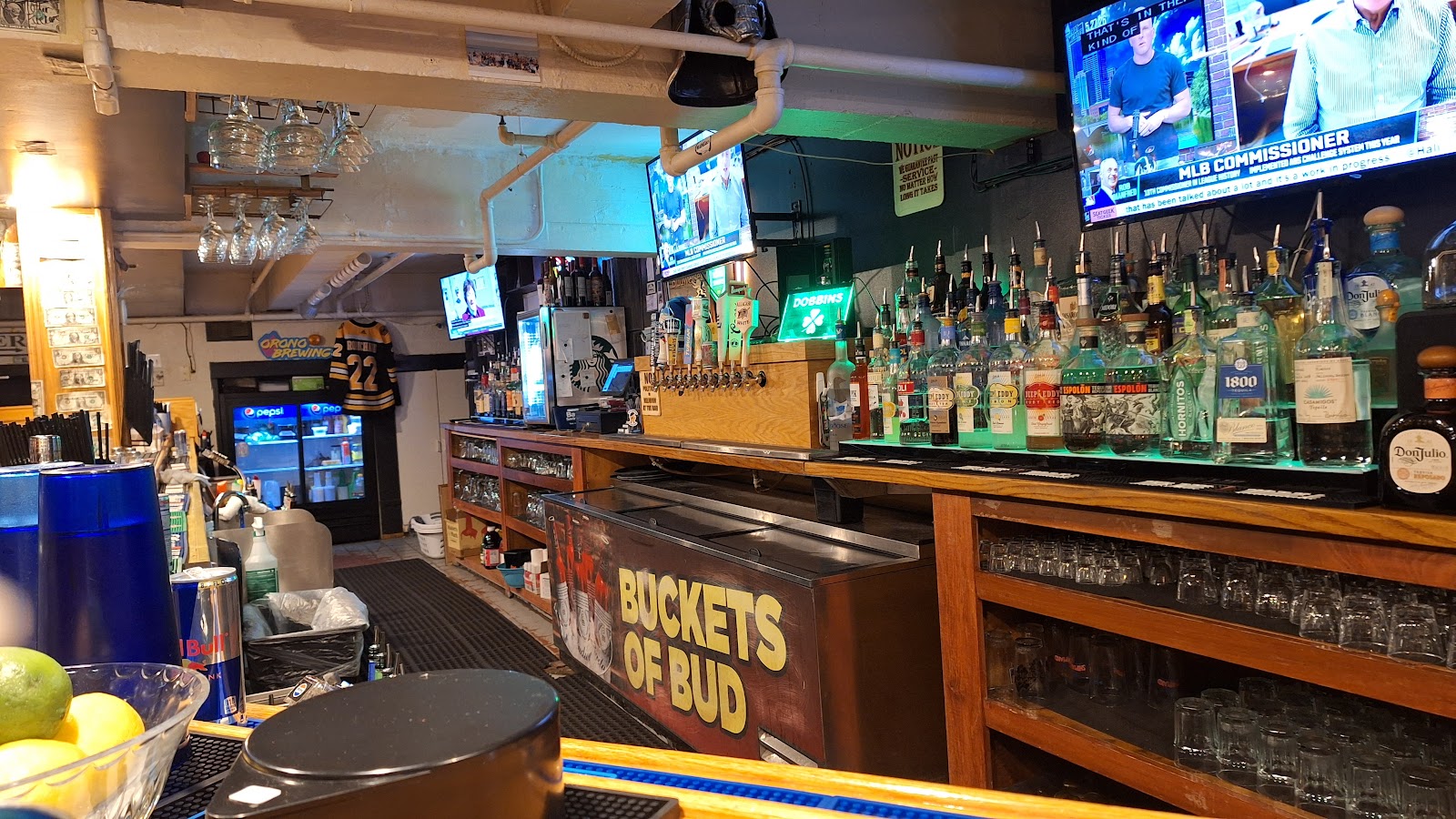 The bar counter with beer taps, a wall of bottles and TVs above a Buckets of Bud sign.