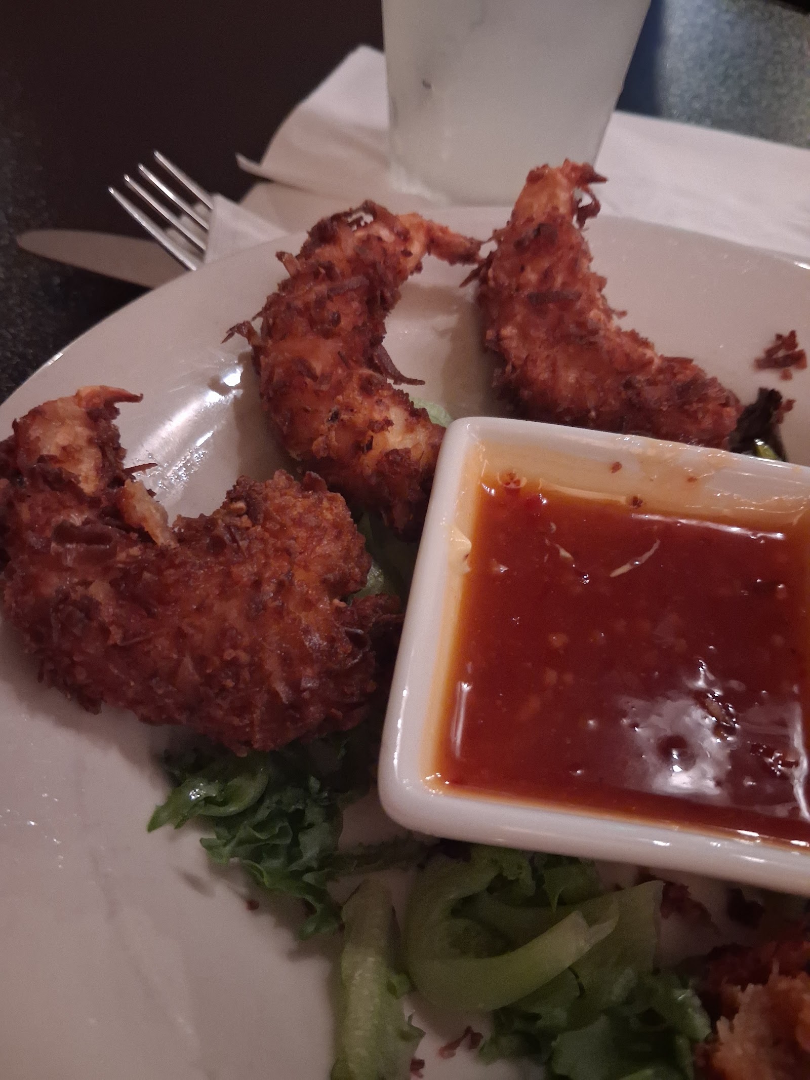 Three golden coconut-crusted shrimp beside a dish of red sweet chili sauce.