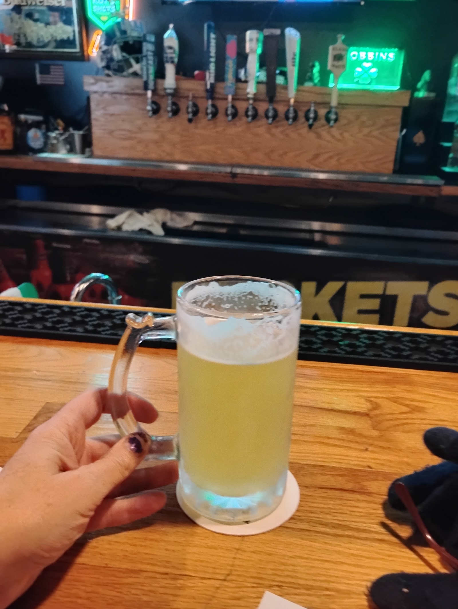 A frosty glass mug of draft beer held at the bar in front of a row of taps.