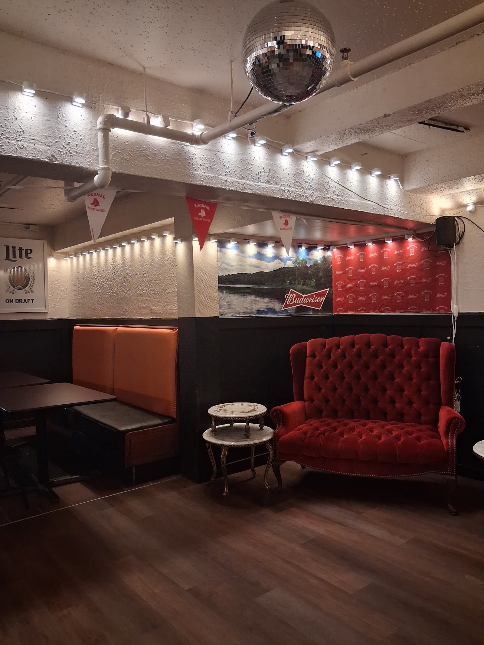 A red velvet couch and orange booths under a disco ball and string lights.