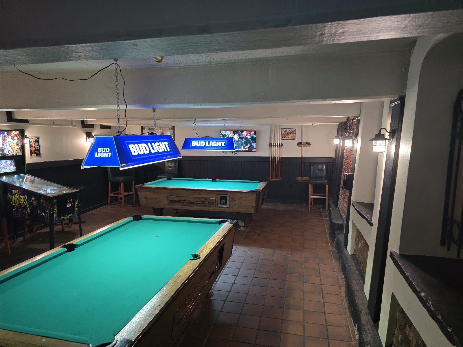 Two pool tables under Bud Light lamps with a pinball machine along the wall.
