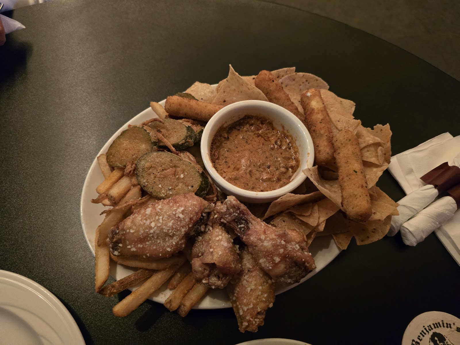 A loaded appetizer platter of wings, fried pickles, chips and fries around a bowl of dip.